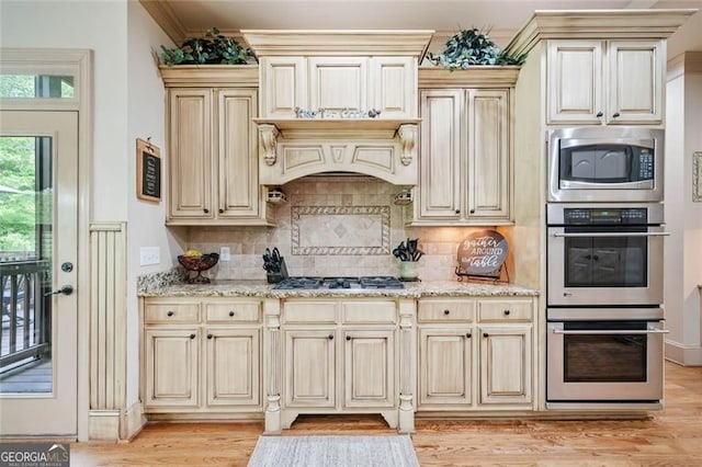 kitchen with light stone countertops, cream cabinets, light wood finished floors, backsplash, and stainless steel appliances