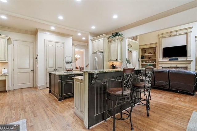kitchen with crown molding, stainless steel refrigerator, a kitchen island, a breakfast bar area, and cream cabinets