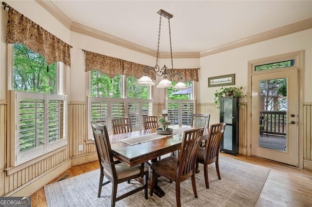 dining space featuring visible vents, a wainscoted wall, light wood finished floors, ornamental molding, and a decorative wall