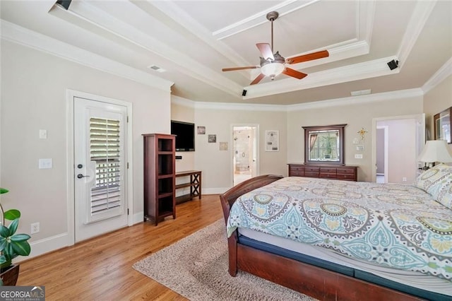bedroom with baseboards, ornamental molding, a raised ceiling, and wood finished floors