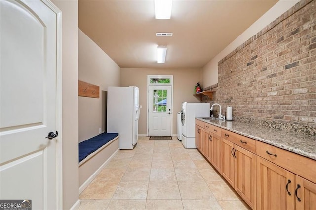 laundry room featuring independent washer and dryer, brick wall, visible vents, a sink, and light tile patterned floors