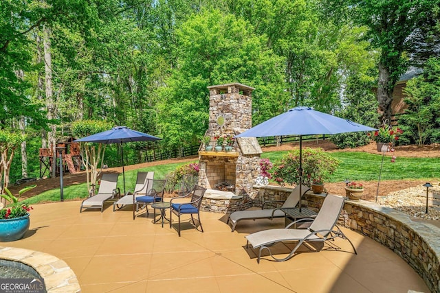 view of patio / terrace featuring an outdoor stone fireplace, a playground, and fence