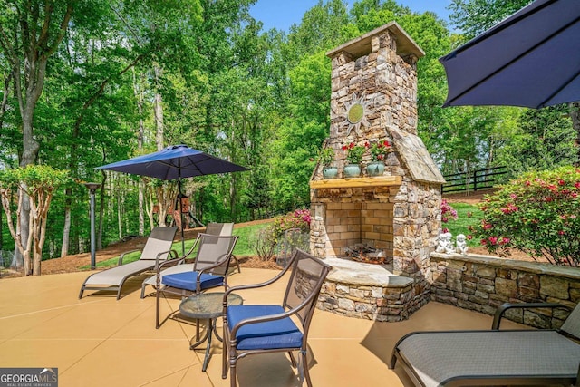 view of patio / terrace with an outdoor stone fireplace, fence, and a playground
