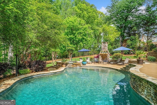 view of pool with an outdoor stone fireplace, a patio area, fence, and a pool with connected hot tub
