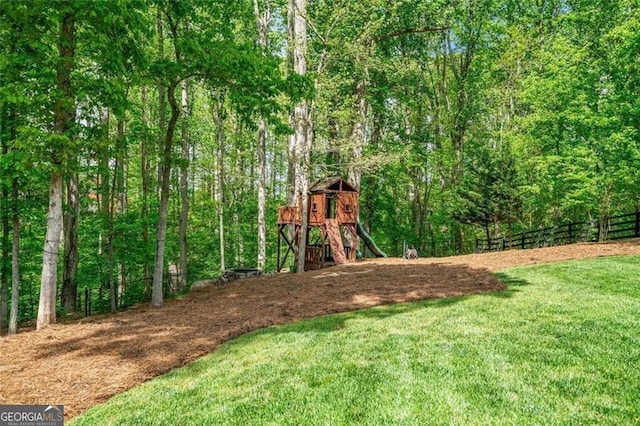 view of jungle gym with a lawn, fence, and a wooded view