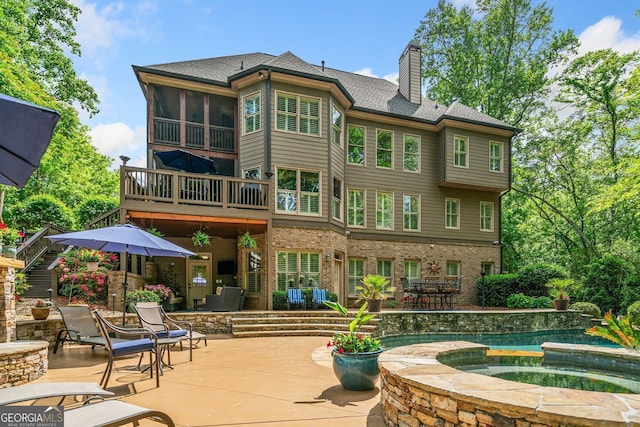 back of property with a patio area, a balcony, a chimney, and an in ground hot tub