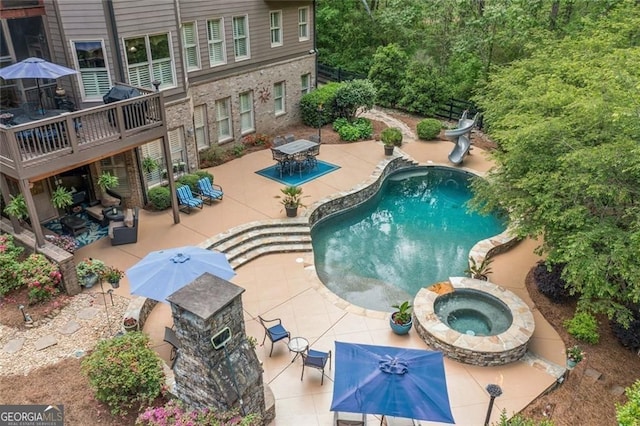 outdoor pool featuring outdoor dining area, an in ground hot tub, a water slide, and a patio area
