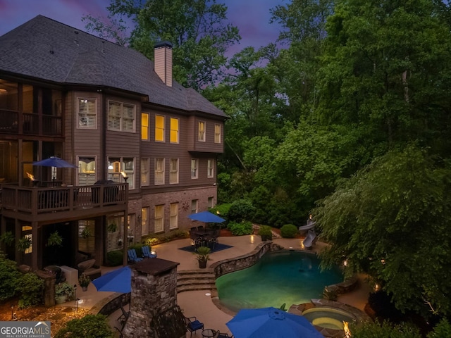 back of house at dusk featuring a pool with connected hot tub, a chimney, and a patio area