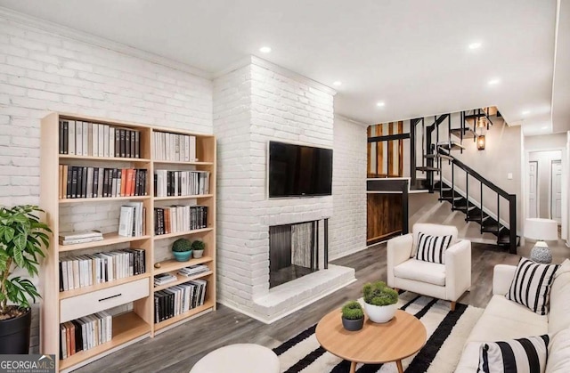 living area with stairway, brick wall, recessed lighting, a fireplace, and wood finished floors
