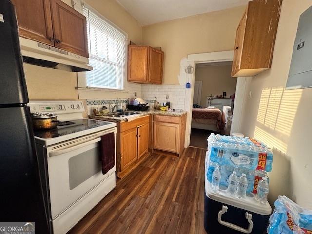 kitchen with freestanding refrigerator, under cabinet range hood, a sink, white electric range oven, and dark wood-type flooring
