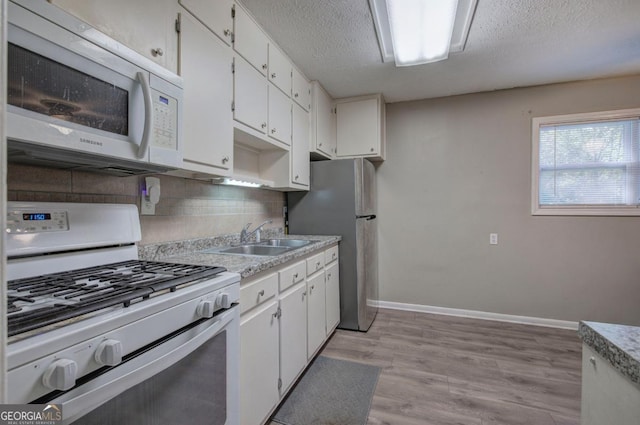 kitchen with a sink, decorative backsplash, light wood-style flooring, white cabinetry, and white appliances