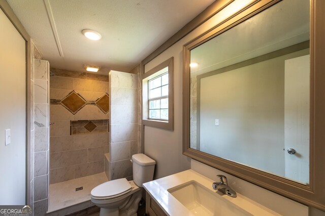 bathroom featuring toilet, a tile shower, and vanity