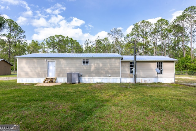 rear view of property with central AC unit, a yard, entry steps, and metal roof