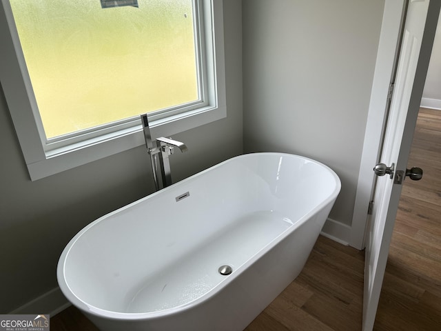 full bath featuring wood finished floors, a soaking tub, and baseboards