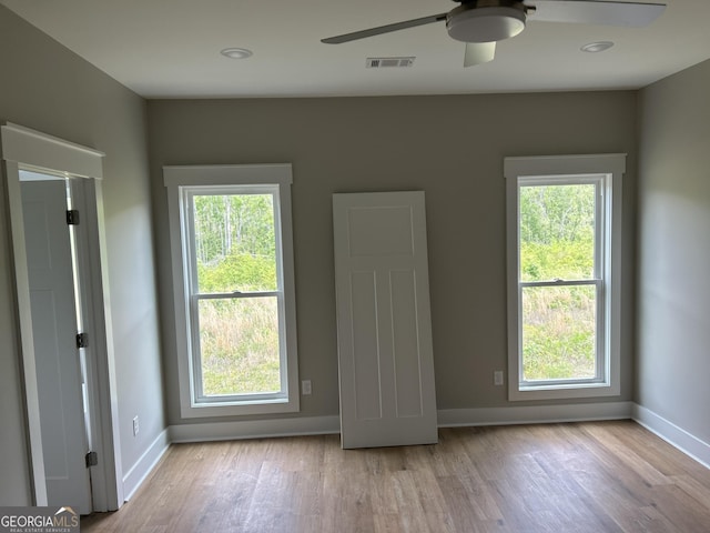 unfurnished room featuring a healthy amount of sunlight, visible vents, wood finished floors, and a ceiling fan