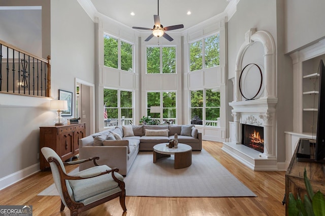 living area with a towering ceiling, a ceiling fan, a high end fireplace, healthy amount of natural light, and ornamental molding