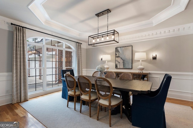 dining space with a tray ceiling, crown molding, wood finished floors, a wainscoted wall, and a decorative wall