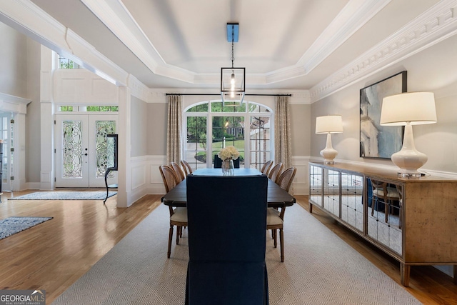 dining room with a raised ceiling, healthy amount of natural light, wood finished floors, crown molding, and a decorative wall