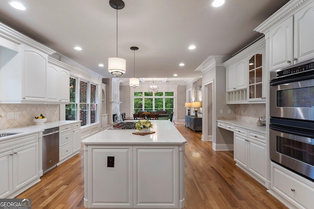 kitchen with stainless steel appliances, a kitchen island, white cabinets, recessed lighting, and glass insert cabinets