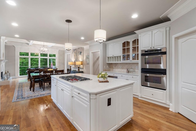 kitchen with appliances with stainless steel finishes, a kitchen island, glass insert cabinets, white cabinets, and light wood-style flooring