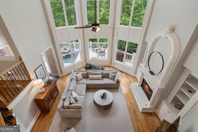 living room featuring a towering ceiling, light wood-type flooring, a lit fireplace, and a ceiling fan