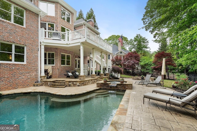 rear view of property with brick siding, a balcony, a patio area, and an outdoor pool