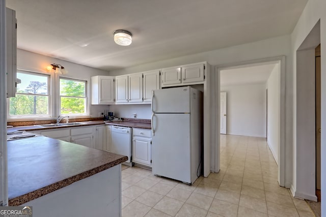 kitchen with dark countertops, a sink, light tile patterned floors, white cabinets, and white appliances