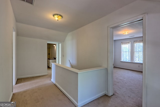 hallway with light carpet, baseboards, an upstairs landing, lofted ceiling, and visible vents