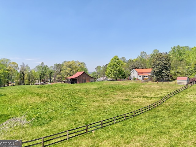 view of yard with fence, a barn, an outdoor structure, and a rural view
