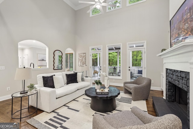 living area with ceiling fan, a fireplace with raised hearth, wood finished floors, and a towering ceiling
