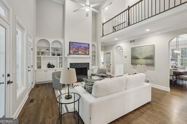 living room featuring a fireplace, arched walkways, visible vents, and a towering ceiling