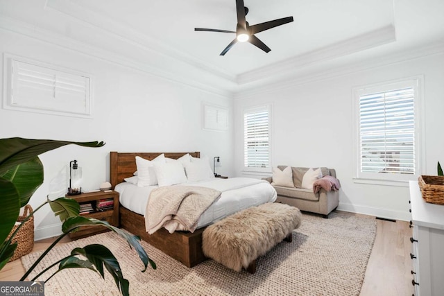 bedroom featuring a raised ceiling, crown molding, light wood finished floors, ceiling fan, and baseboards