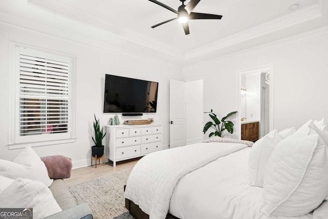 bedroom with a raised ceiling, light wood-style flooring, ornamental molding, connected bathroom, and ceiling fan