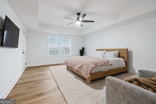 bedroom with a raised ceiling, light wood-type flooring, baseboards, and a ceiling fan