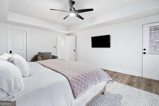 bedroom featuring wood finished floors, baseboards, a tray ceiling, and ceiling fan