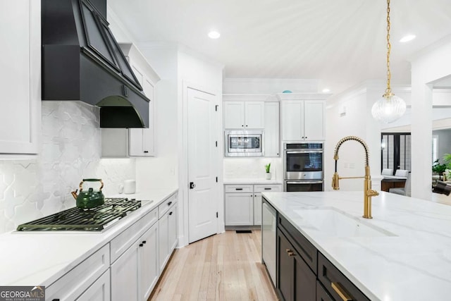 kitchen with appliances with stainless steel finishes, a sink, premium range hood, white cabinets, and pendant lighting
