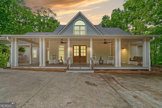 back of property at dusk featuring a porch, ceiling fan, a shingled roof, and french doors