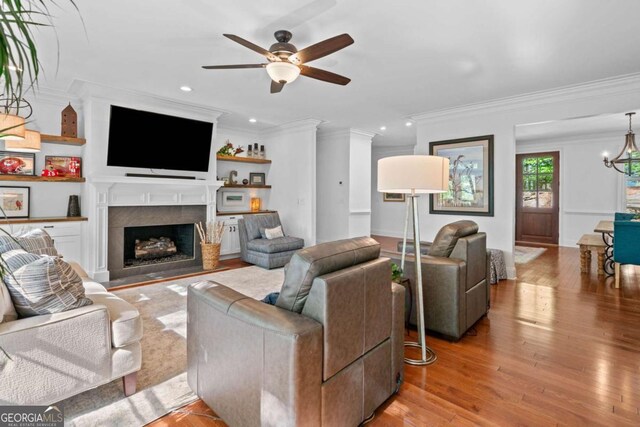 living area with recessed lighting, a fireplace with flush hearth, light wood-style floors, ornamental molding, and ceiling fan with notable chandelier