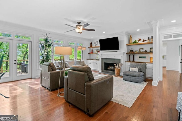 living area featuring wood-type flooring, a ceiling fan, a fireplace with flush hearth, and french doors