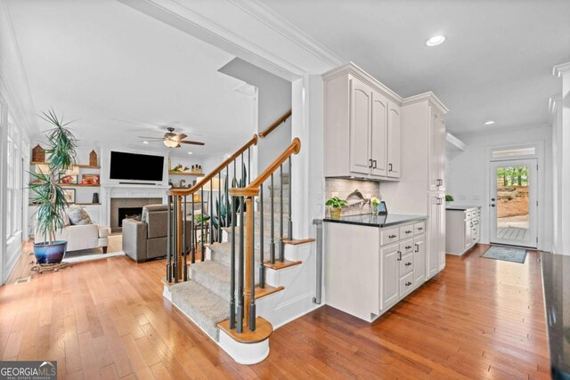 staircase with hardwood / wood-style flooring, ceiling fan, crown molding, and a fireplace