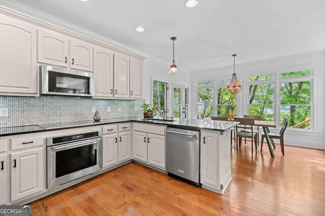 kitchen featuring light wood-style flooring, a sink, appliances with stainless steel finishes, a peninsula, and backsplash