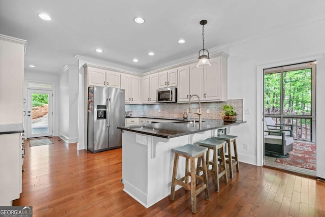 kitchen featuring a sink, crown molding, a peninsula, appliances with stainless steel finishes, and wood finished floors
