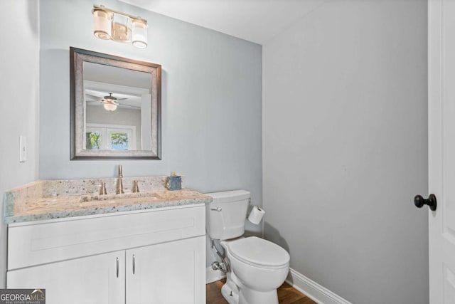 half bath featuring baseboards, wood finished floors, toilet, and vanity