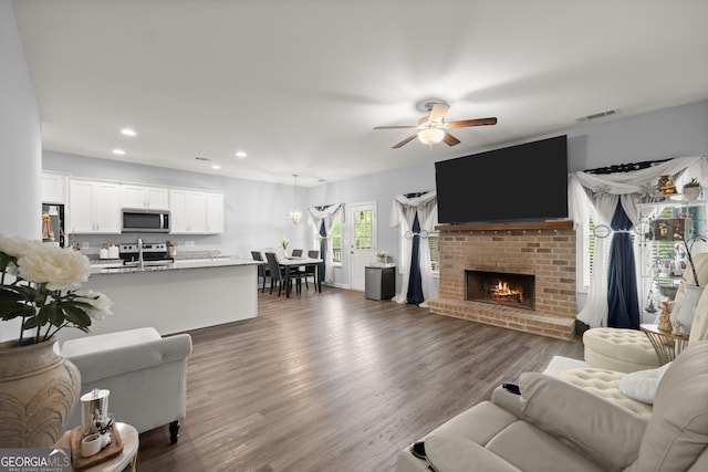 living area featuring recessed lighting, a brick fireplace, ceiling fan, visible vents, and wood finished floors