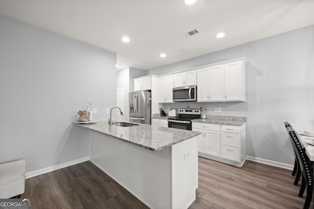 kitchen with white cabinets, a sink, appliances with stainless steel finishes, baseboards, and a peninsula