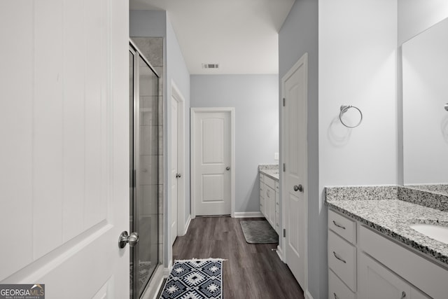 full bath with a stall shower, two vanities, visible vents, and wood finished floors