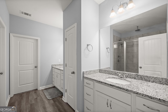 full bathroom featuring a sink, visible vents, a stall shower, two vanities, and wood finished floors
