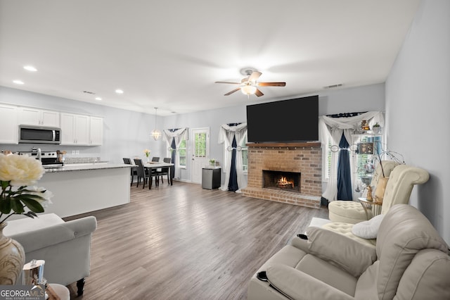living room featuring recessed lighting, wood finished floors, ceiling fan, a brick fireplace, and visible vents