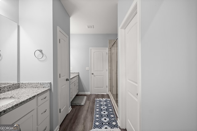 bathroom featuring a sink, visible vents, a stall shower, two vanities, and wood finished floors