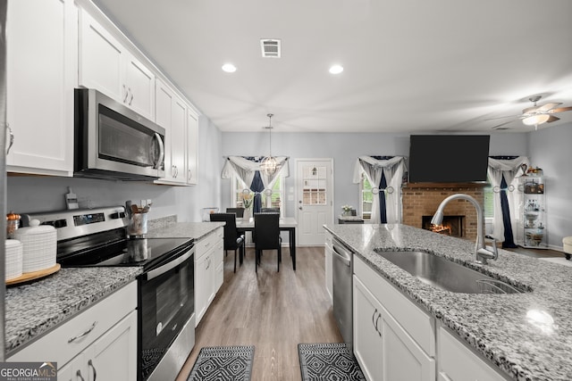 kitchen with a sink, stainless steel appliances, a brick fireplace, ceiling fan, and white cabinetry